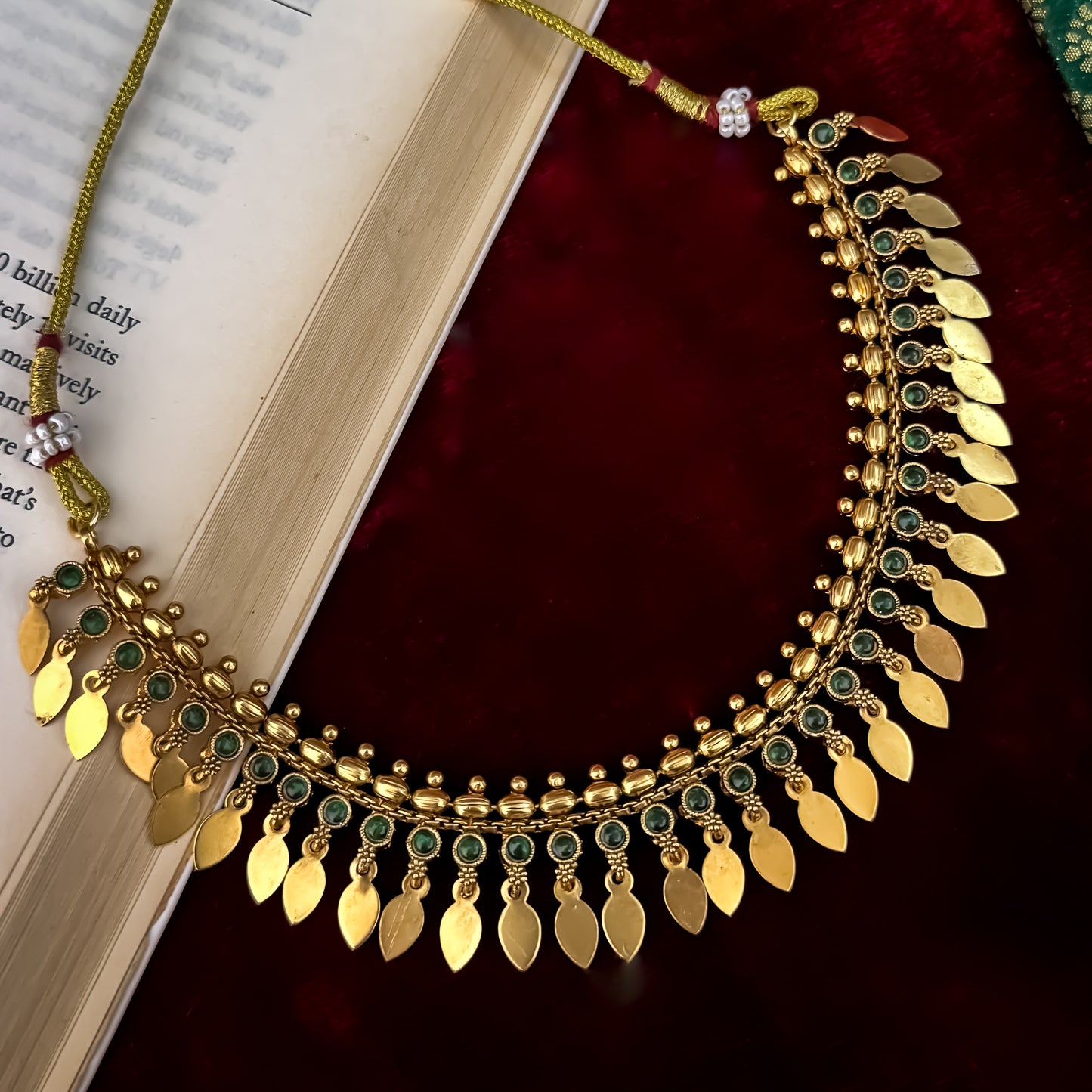 Kaira Temple premium antique gold choker necklace featuring a linear track of round emerald green kemp stones a top row of gold beads a bottom cascading fringe of flat coin leaf drops and matching earrings