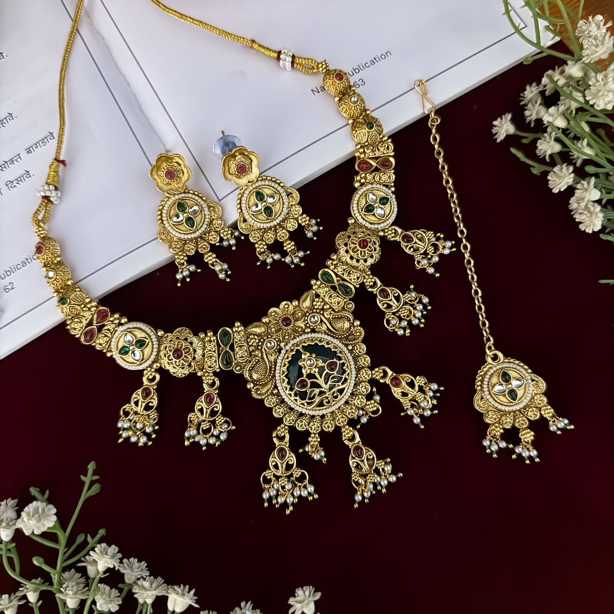 premium antique gold kundan necklace set featuring a multi strand tracking of white pearls and green beads a large central circular medallion with red and green stones and matching rectangular tiered drop earrings