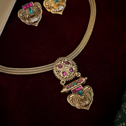 Traditional South Indian gold wedding necklace and earring set displayed flat lay over a dark red velvet background next to an open book and green silk fabric