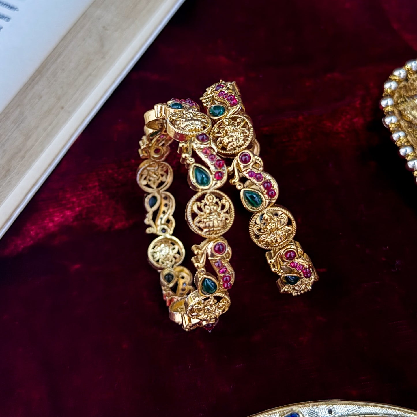 premium antique gold temple bangles featuring continuous rows of sculpted goddess lakshmi motifs square green stones and maroon halos