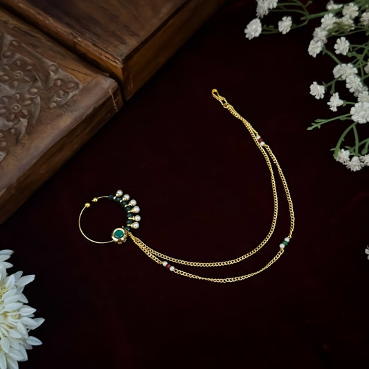 Traditional Indian wedding gold and ruby pink stone statement non pierced press on bridal nose ring nath with cascading sahara hair links displayed flat lay resting on a rich dark red maroon fabric backdrop