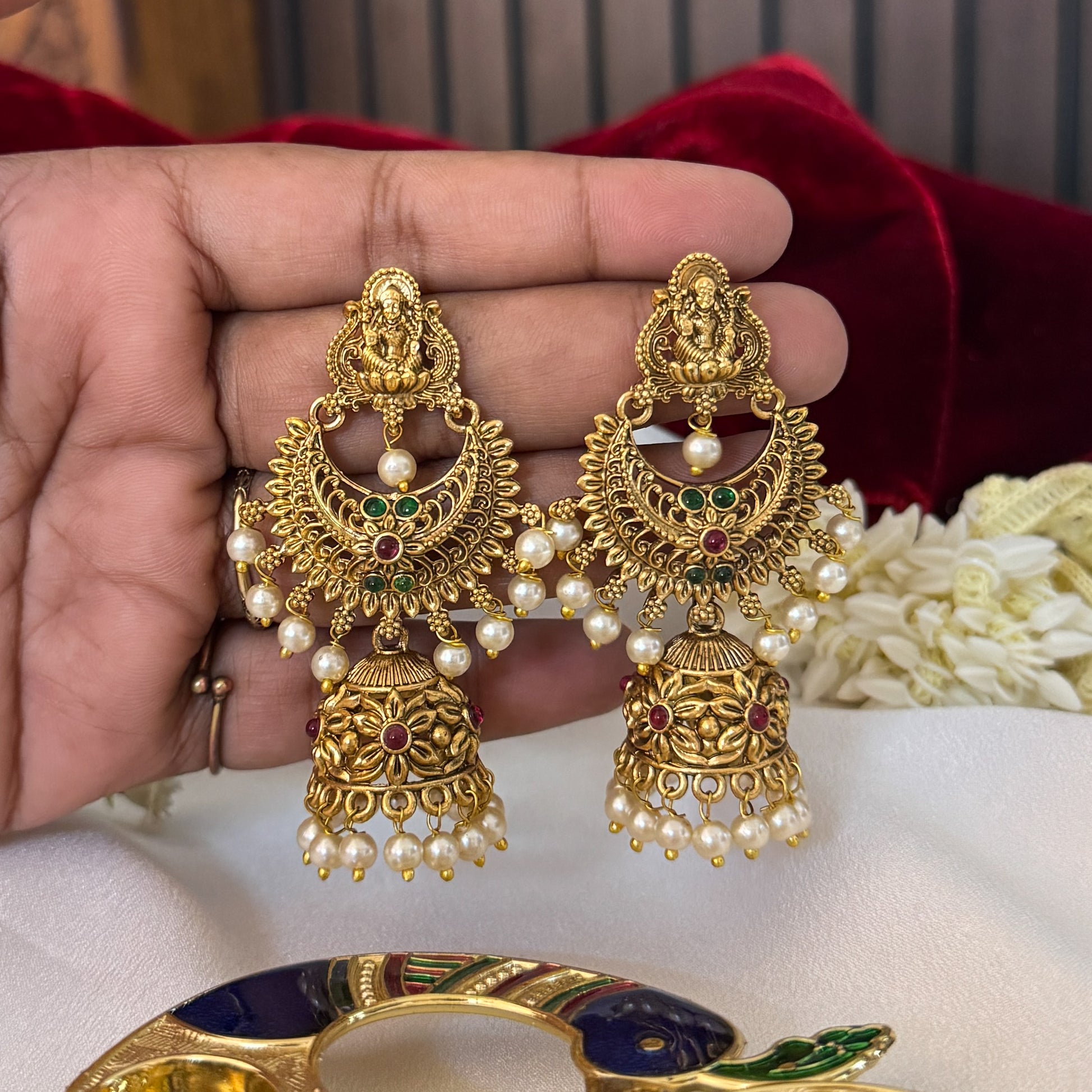 Chandrika Kemp Stone premium antique gold temple earrings featuring leaf shaped goddess lakshmi studs a crescent chandbali medallion frame with red and green stones and an engraved dome jhumka cup with a dense white seed pearl fringe