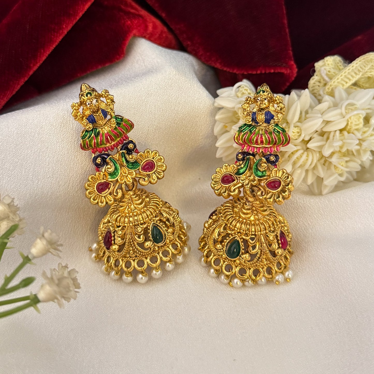 Gaurika premium antique gold temple earrings featuring goddess lakshmi studs twin peacock links with red and green meenakari enamel and an engraved dome jhumka cup with a dense white seed pearl fringe