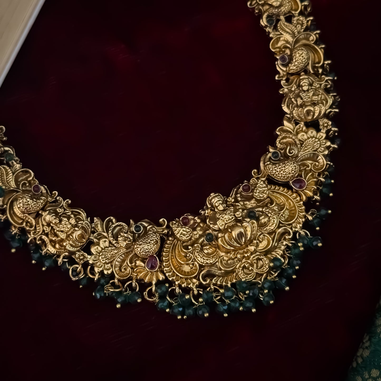 Shreedha premium antique gold temple necklace set featuring a large sculpted goddess lakshmi lotus medallion peacock motifs and green bead fringe with matching earrings