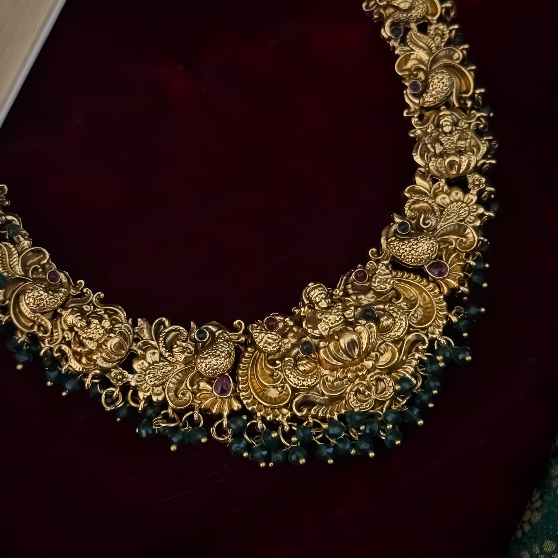 Shreedha premium antique gold temple necklace set featuring a large sculpted goddess lakshmi lotus medallion peacock motifs and green bead fringe with matching earrings