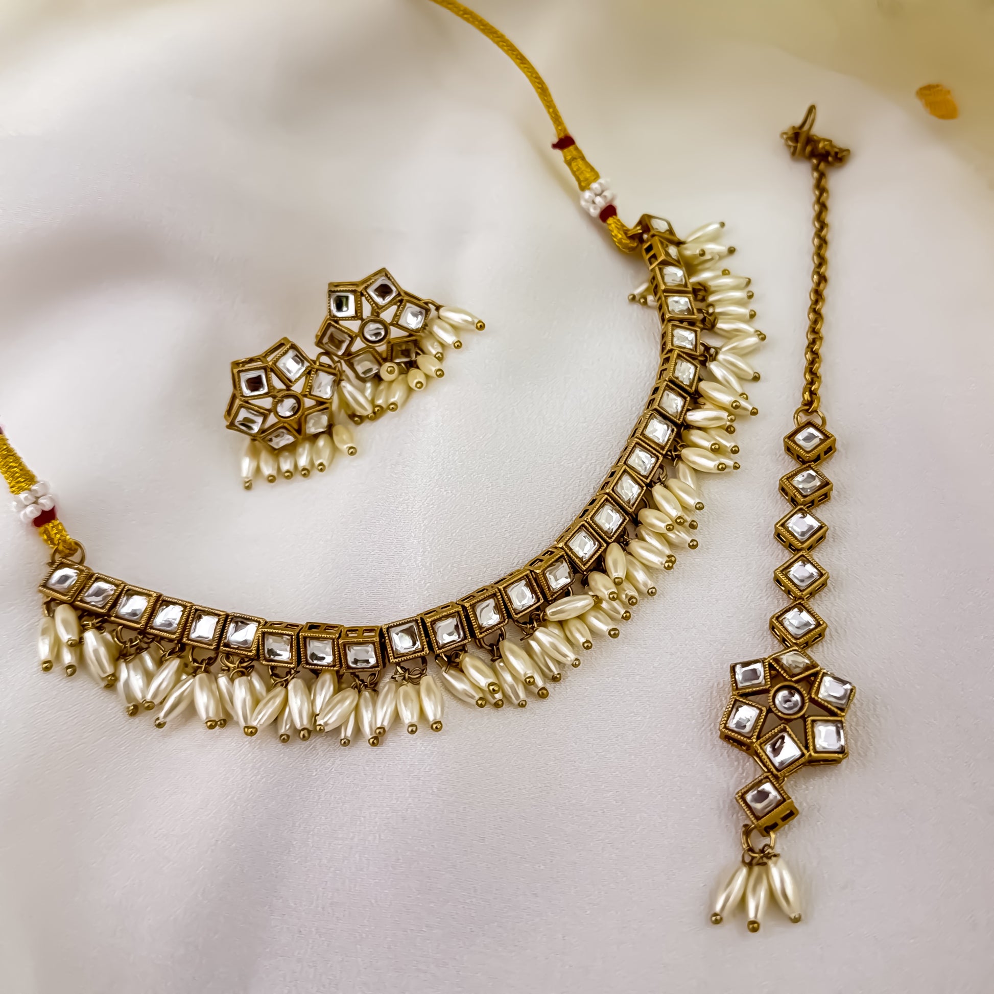 Yashvi premium antique gold kundan sleek collar necklace set featuring a linear linked tracking of clear dabi stones and a dense cascading fringe of white rice pearls with matching hexagonal stud earrings and maang tikka