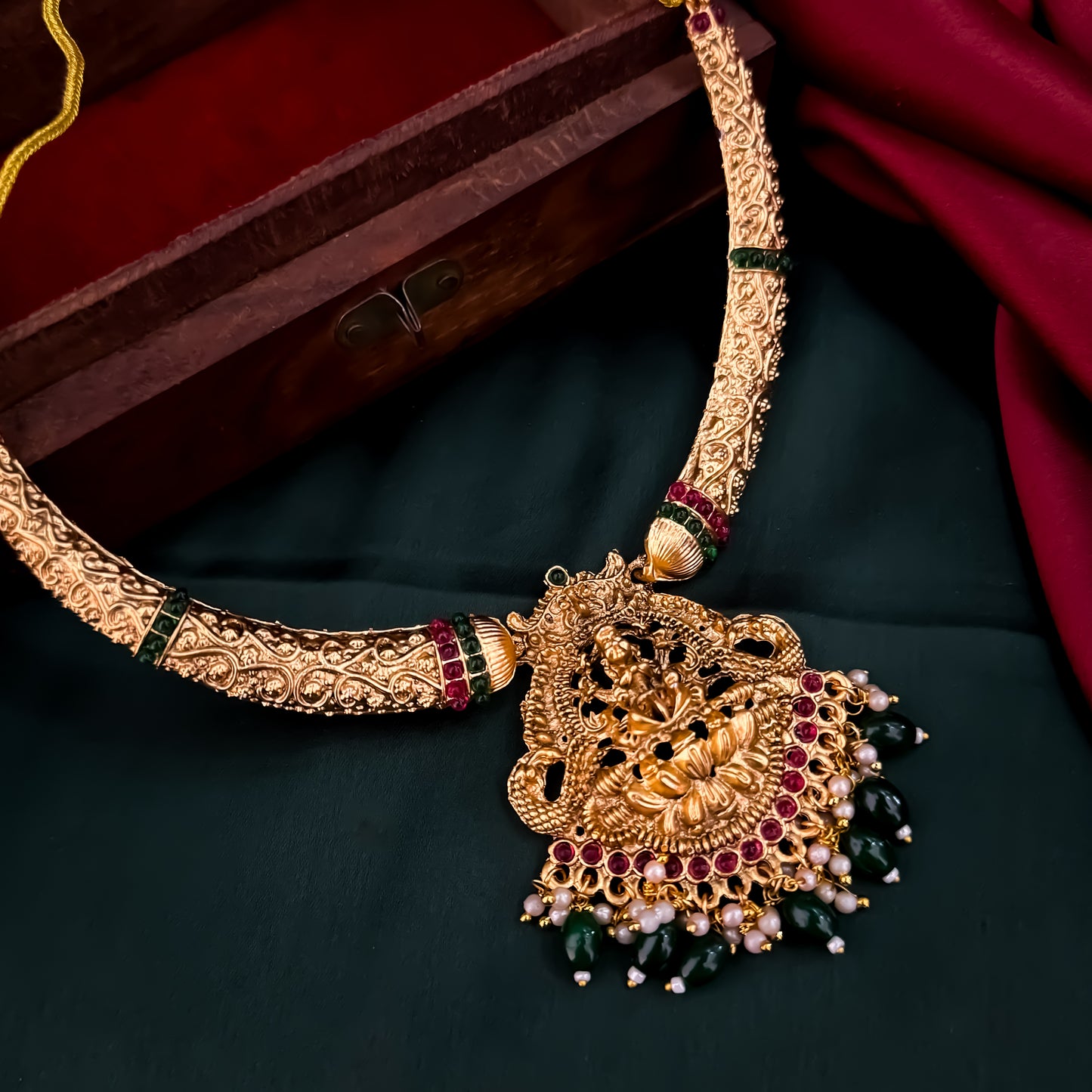 Bhavika temple jewelry hasli necklace set featuring a matte gold goddess lakshmi pendant with ruby stones and hanging green crystal drops