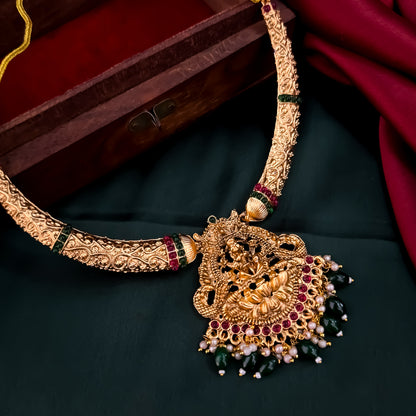 Bhavika temple jewelry hasli necklace set featuring a matte gold goddess lakshmi pendant with ruby stones and hanging green crystal drops