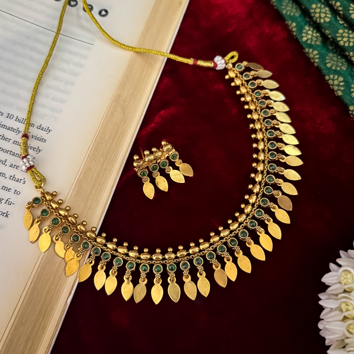 Kaira Temple premium antique gold choker necklace featuring a linear track of round emerald green kemp stones a top row of gold beads a bottom cascading fringe of flat coin leaf drops and matching earrings