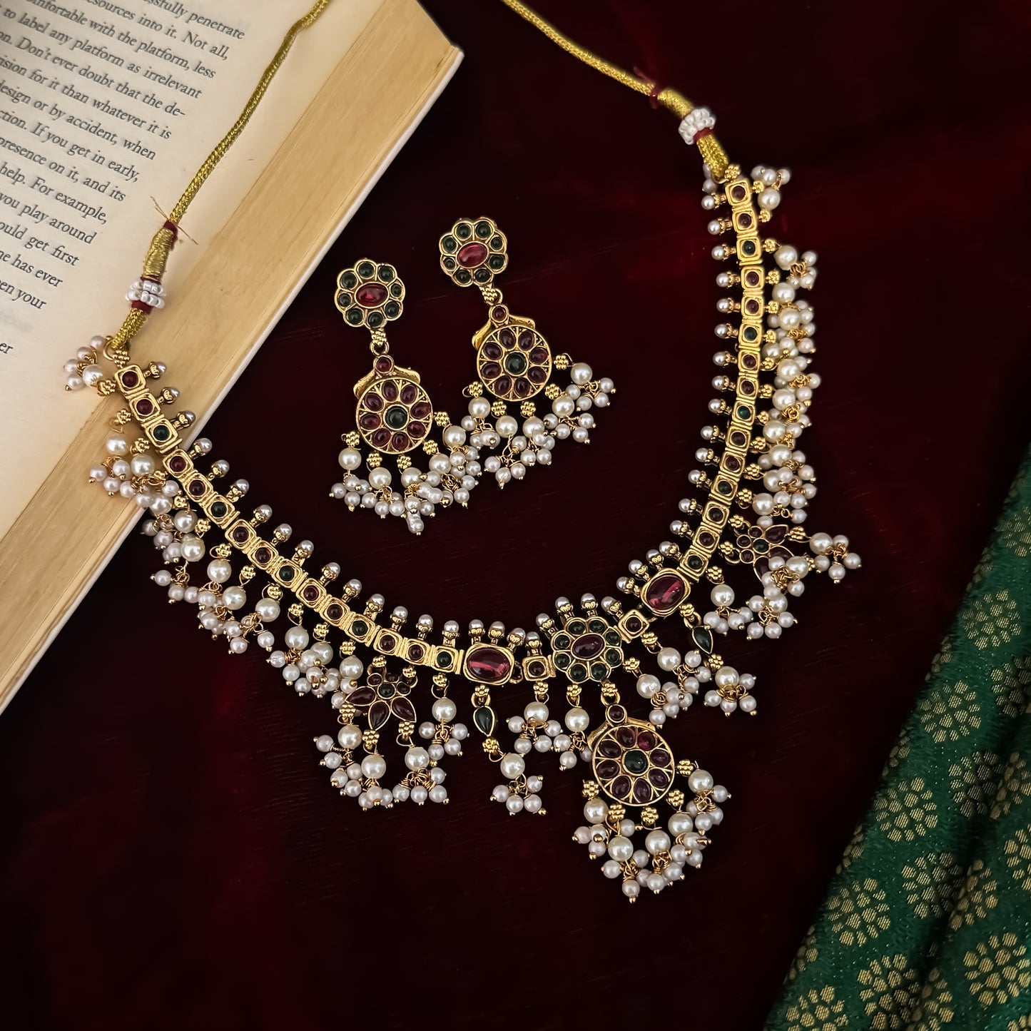 Qavithri premium antique gold temple choker necklace set featuring a guttapusalu multi strand white pearl cluster fringe with clear pink and green kemp stones alongside matching tiered chakra drop earrings