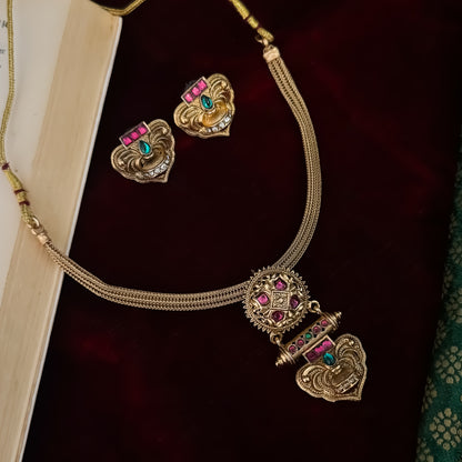 Traditional South Indian gold wedding necklace and earring set displayed flat lay over a dark red velvet background next to an open book and green silk fabric