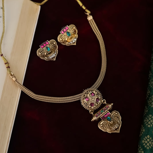 Traditional South Indian gold wedding necklace and earring set displayed flat lay over a dark red velvet background next to an open book and green silk fabric