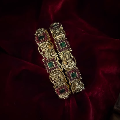 Yashaswini premium antique gold temple bangles featuring continuous rows of sculpted goddess lakshmi motifs square green stones and maroon halos