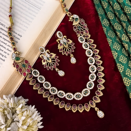 Aarna Temple premium antique gold double layer choker necklace featuring two linked tracks of concentric round green stones and a cascading bottom fringe of ruby red teardrop stones alongside matching chandelier earrings