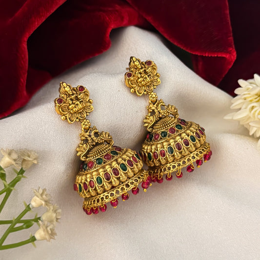 Nishika Temple Motif Jhumka Earrings featuring premium antique gold Goddess Lakshmi and peacock top studs holding a wide flared dome cup with a dense cascading white seed pearl fringe
