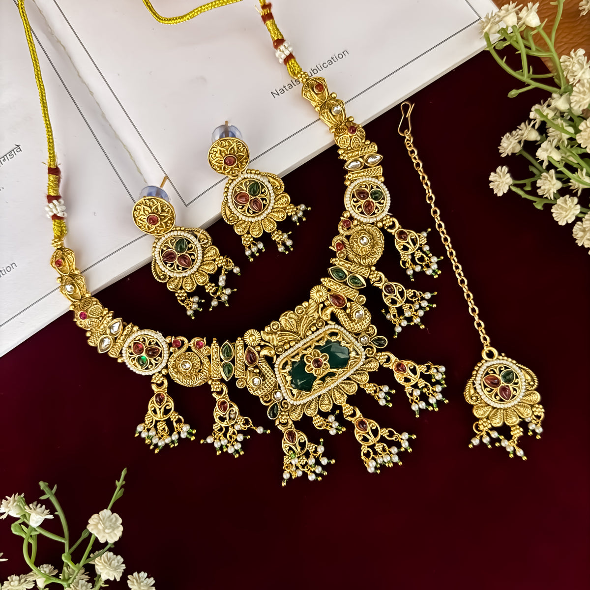 premium antique gold kundan necklace set featuring a multi strand tracking of white pearls and green beads a large central circular medallion with red and green stones and matching rectangular tiered drop earrings