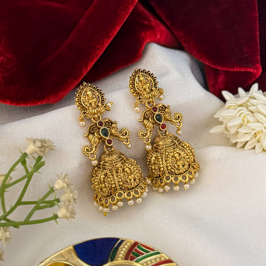 Tapasya Kemp Stone premium antique gold temple earrings featuring leaf shaped goddess lakshmi studs twin peacock links with red and green stones and an engraved dome jhumka cup with a dense white seed pearl fringe
