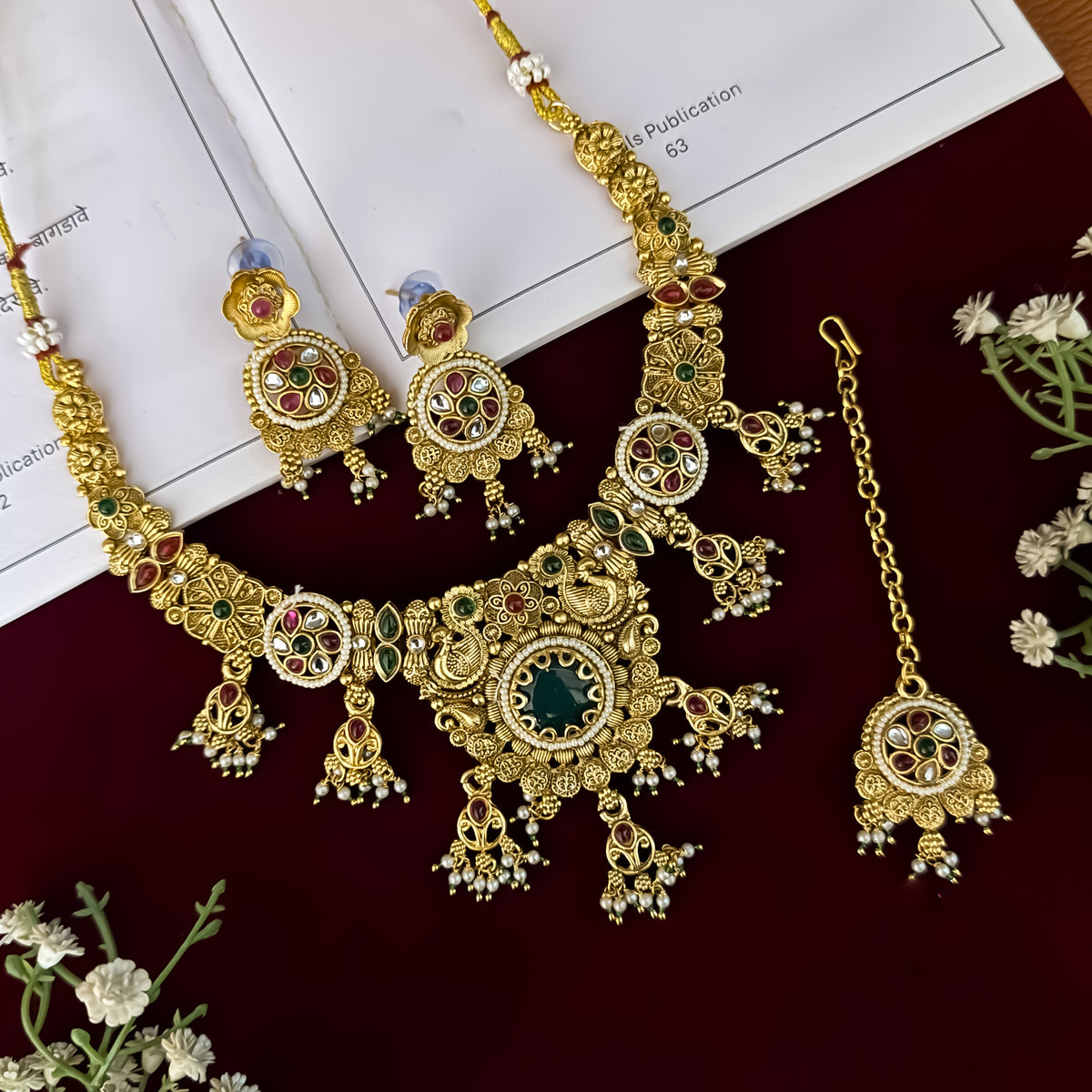 premium antique gold kundan necklace set featuring a multi strand tracking of white pearls and green beads a large central circular medallion with red and green stones and matching rectangular tiered drop earrings