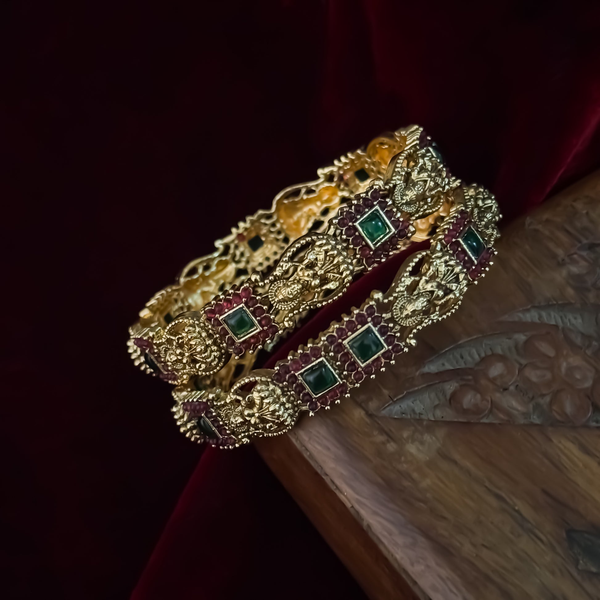 Yashaswini premium antique gold temple bangles featuring continuous rows of sculpted goddess lakshmi motifs square green stones and maroon halos