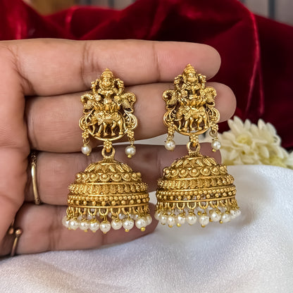 Temple Motif Jhumka Earrings featuring premium antique gold Goddess Lakshmi and peacock top studs holding a wide flared dome cup with a dense cascading white seed pearl fringe