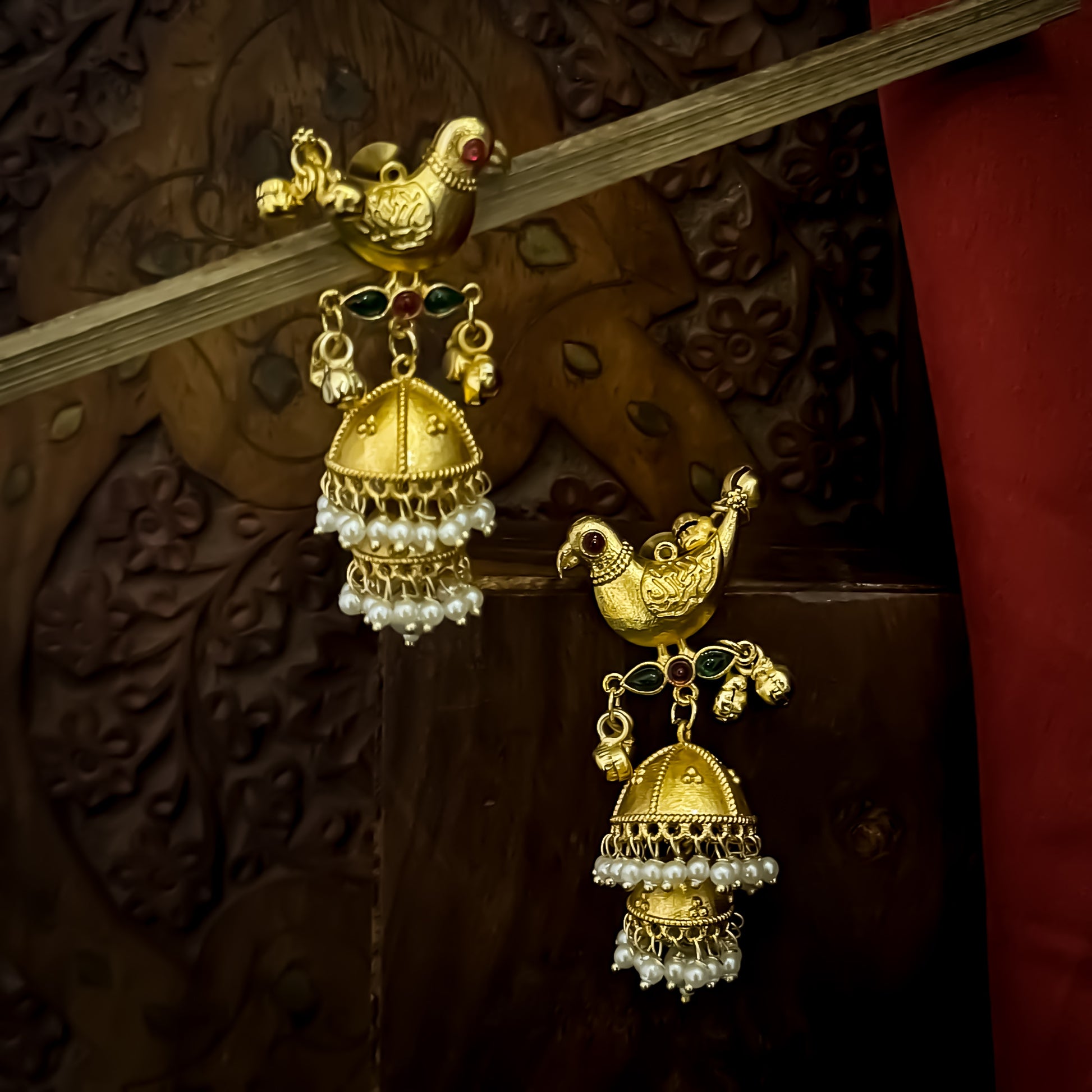 Totapari premium kashmiri brass jhumka earrings featuring sculpted gold peacock studs red and green stone links and three tiered pearl domes