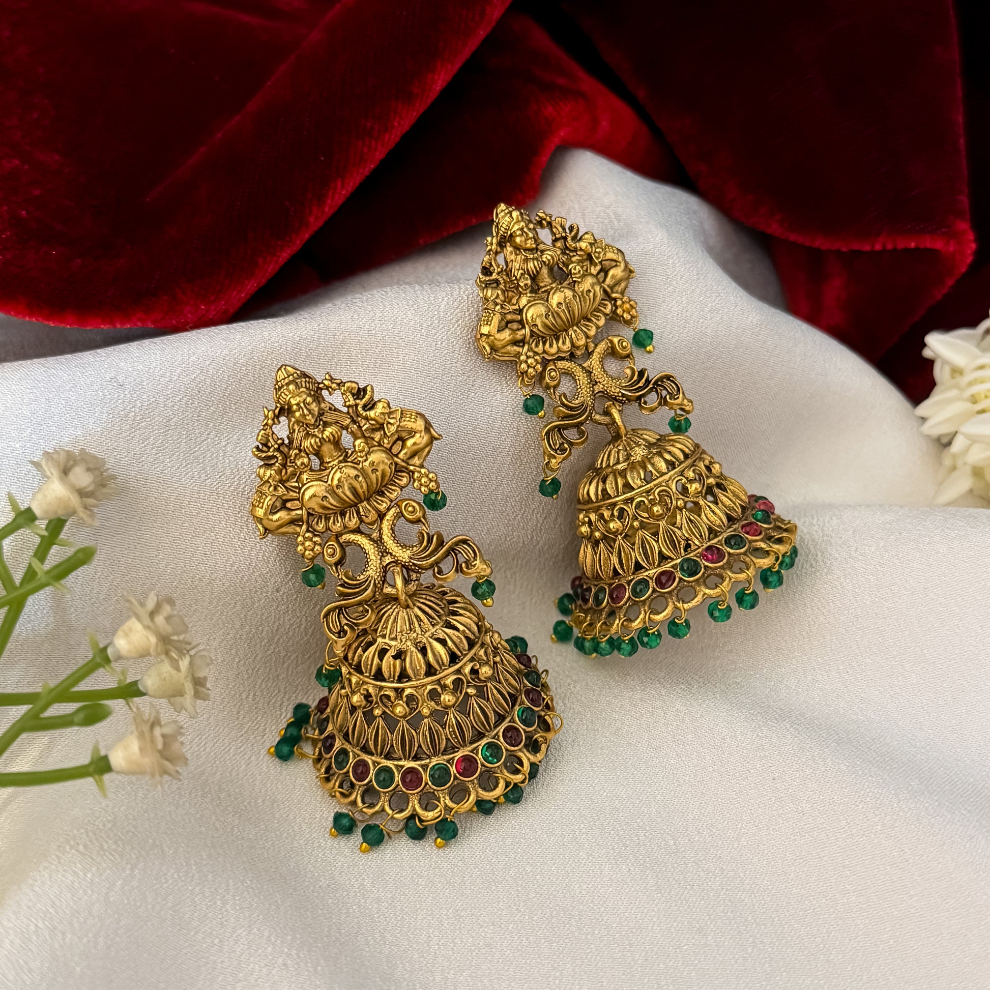 Aadya Kemp Stone premium antique gold temple earrings featuring goddess lakshmi studs twin peacock links with red and green stones and an engraved dome jhumka cup with a dense white seed pearl fringe