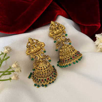 Aadya Kemp Stone premium antique gold temple earrings featuring goddess lakshmi studs twin peacock links with red and green stones and an engraved dome jhumka cup with a dense white seed pearl fringe