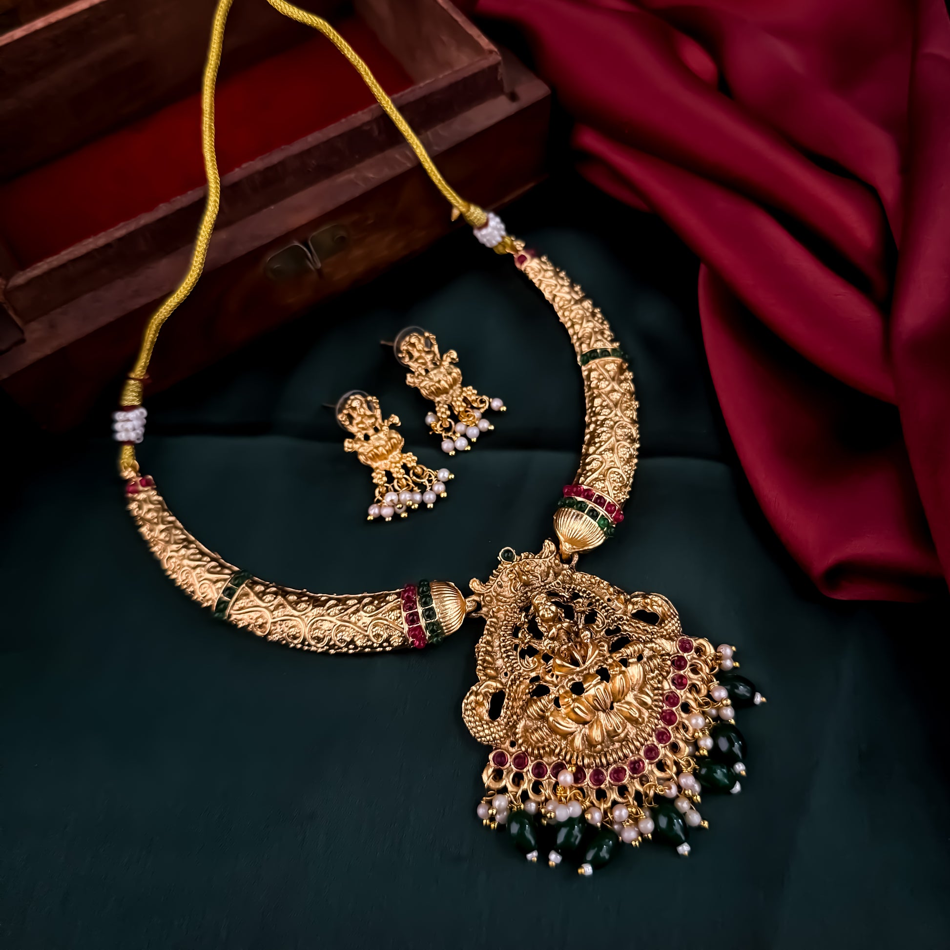 Bhavika temple jewelry hasli necklace set featuring a matte gold goddess lakshmi pendant with ruby stones and hanging green crystal drops