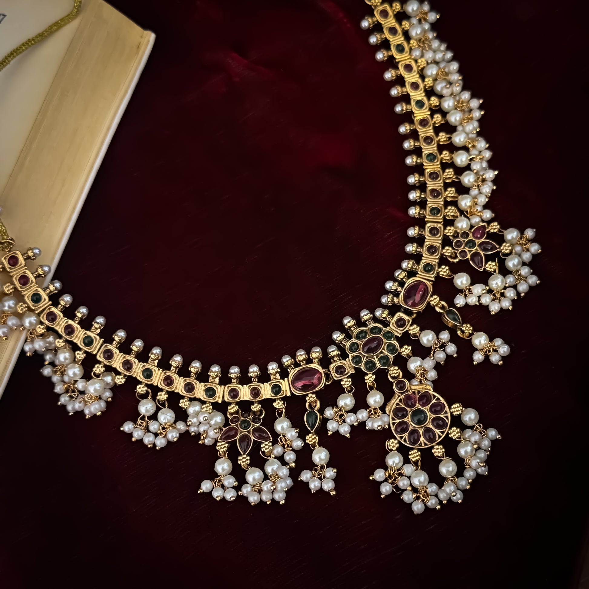 Qavithri premium antique gold temple choker necklace set featuring a guttapusalu multi strand white pearl cluster fringe with clear pink and green kemp stones alongside matching tiered chakra drop earrings