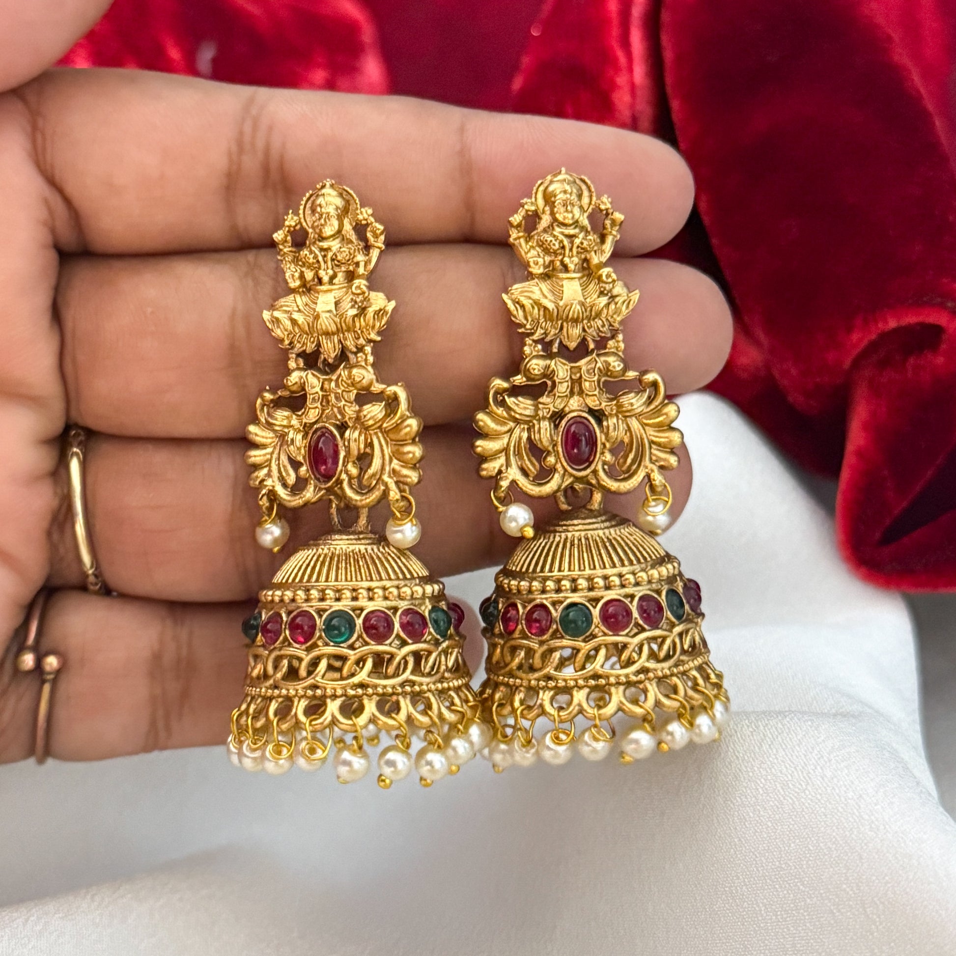 Siddhi Kemp Stone premium antique gold temple earrings featuring goddess lakshmi studs twin peacock links with a central red stone and a wide dome jhumka cup rimmed with multi color stones and a dense white seed pearl fringe
