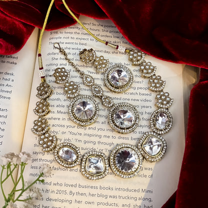 Naira AD premium gold plated necklace set featuring a linear linked tracking of clear mock polki crystal halos a central circular deep wine plum stone medallion matching tiered earrings and a maang tikka