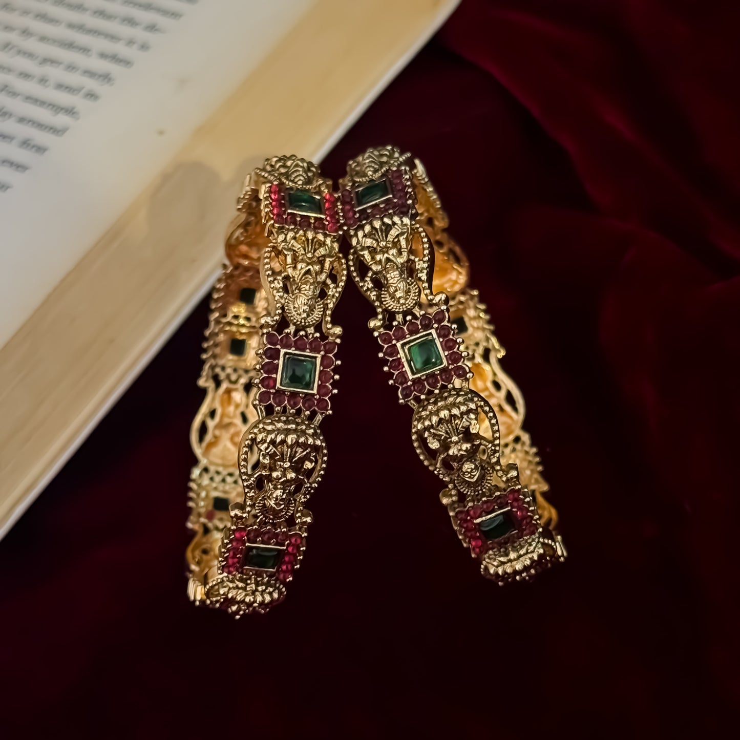 Yashaswini premium antique gold temple bangles featuring continuous rows of sculpted goddess lakshmi motifs square green stones and maroon halos