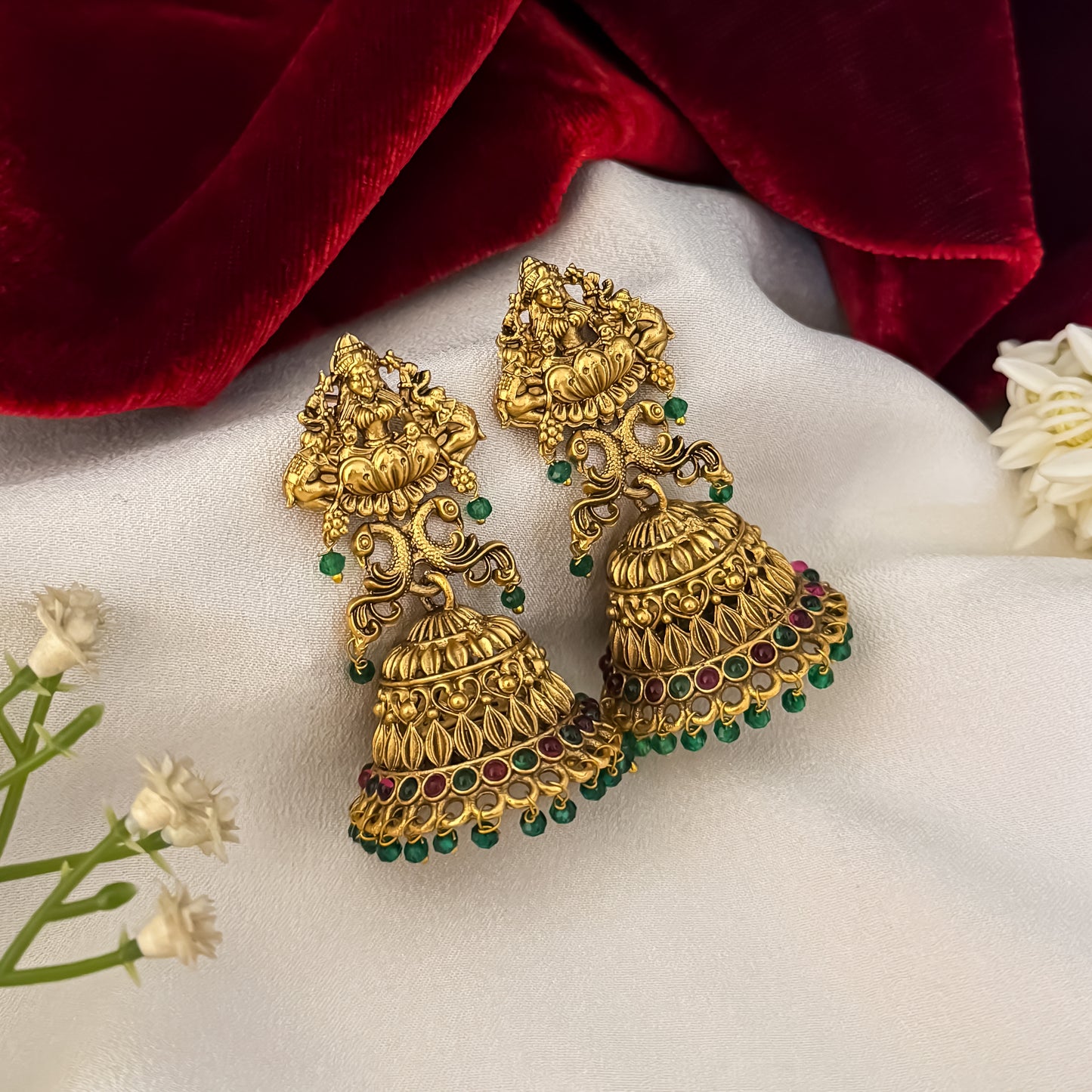 Aadya Kemp Stone premium antique gold temple earrings featuring goddess lakshmi studs twin peacock links with red and green stones and an engraved dome jhumka cup with a dense white seed pearl fringe