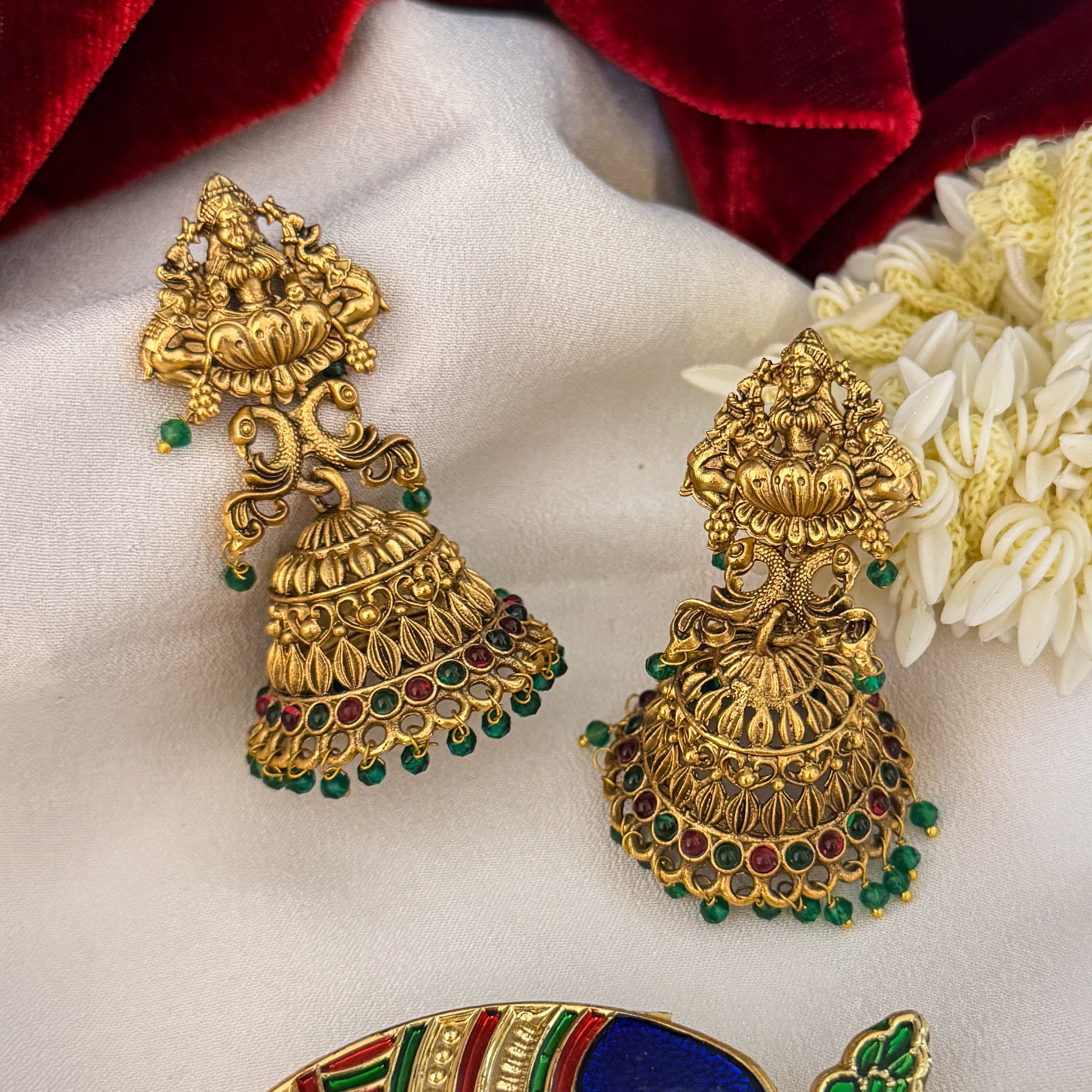 Aadya Kemp Stone premium antique gold temple earrings featuring goddess lakshmi studs twin peacock links with red and green stones and an engraved dome jhumka cup with a dense white seed pearl fringe