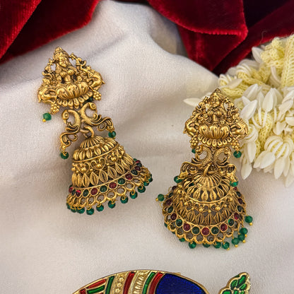 Aadya Kemp Stone premium antique gold temple earrings featuring goddess lakshmi studs twin peacock links with red and green stones and an engraved dome jhumka cup with a dense white seed pearl fringe