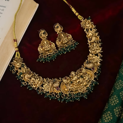 Shreedha premium antique gold temple necklace set featuring a large sculpted goddess lakshmi lotus medallion peacock motifs and green bead fringe with matching earrings