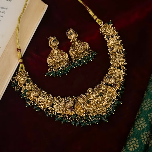Shreedha premium antique gold temple necklace set featuring a large sculpted goddess lakshmi lotus medallion peacock motifs and green bead fringe with matching earrings