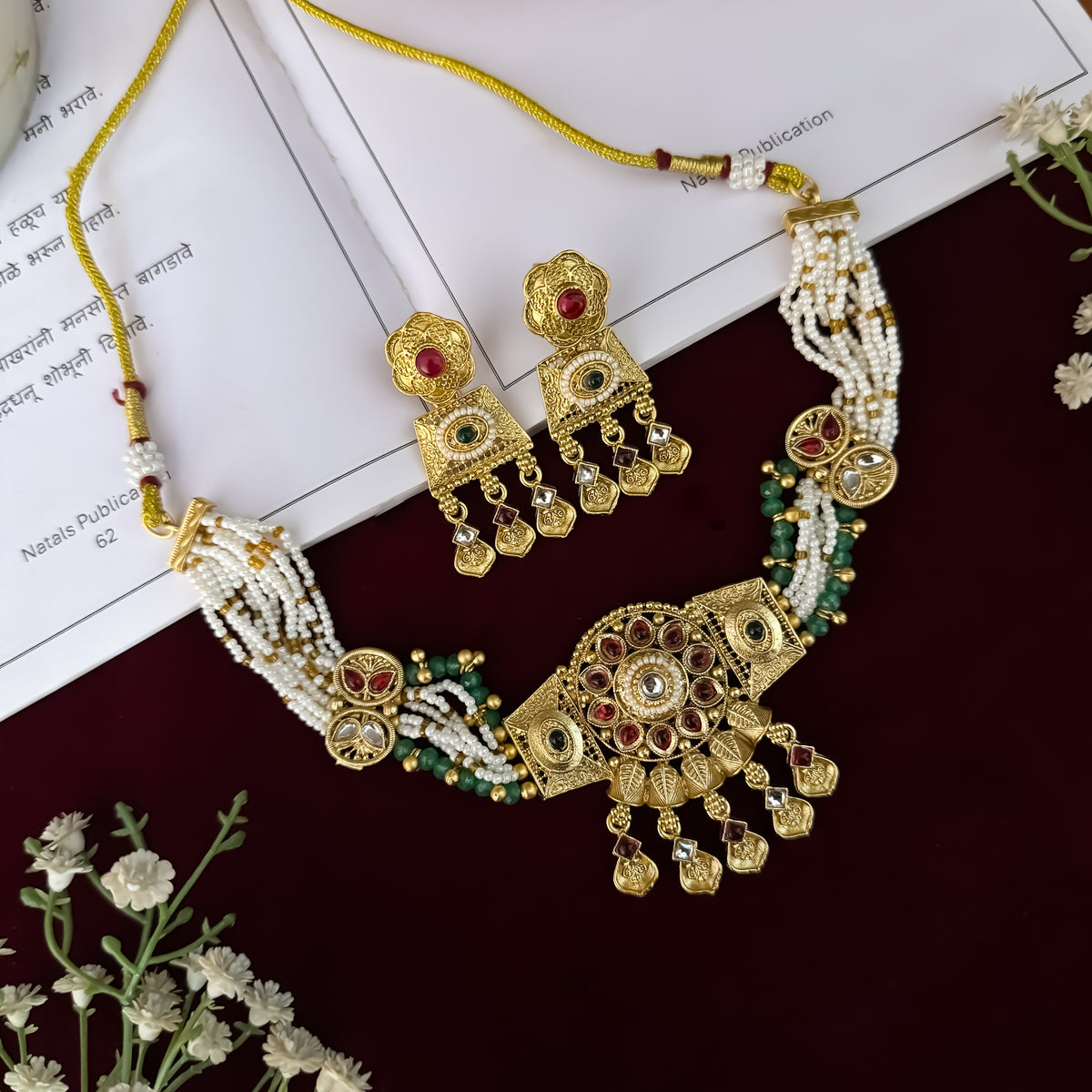 Himangi premium antique gold kundan necklace set featuring a multi strand tracking of white pearls and green beads a large central circular medallion with red and green stones and matching rectangular tiered drop earrings