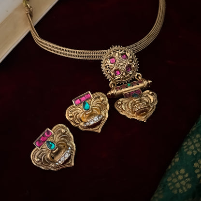 Traditional South Indian gold wedding necklace and earring set displayed flat lay over a dark red velvet background next to an open book and green silk fabric