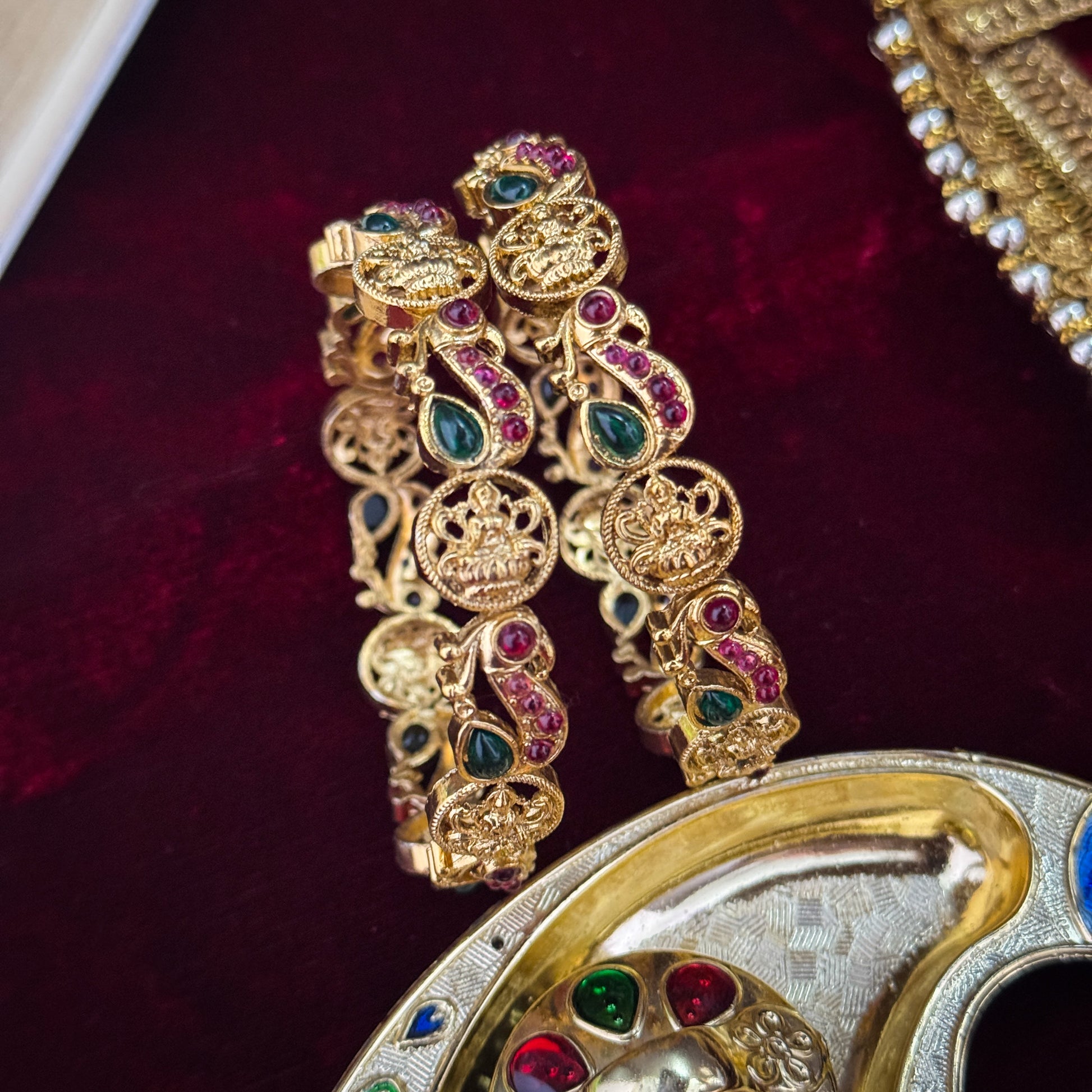 premium antique gold temple bangles featuring continuous rows of sculpted goddess lakshmi motifs square green stones and maroon halos