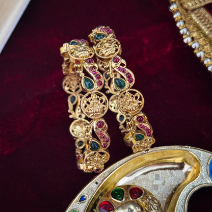 premium antique gold temple bangles featuring continuous rows of sculpted goddess lakshmi motifs square green stones and maroon halos