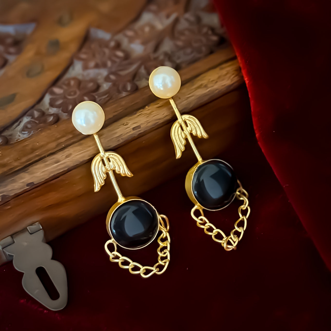 Veena premium brass earrings featuring white pearl studs matte gold leaf stems and round black monalisa stones with looped chain drapes