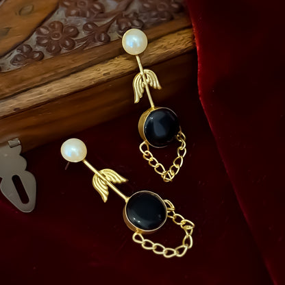 Veena premium brass earrings featuring white pearl studs matte gold leaf stems and round black monalisa stones with looped chain drapes