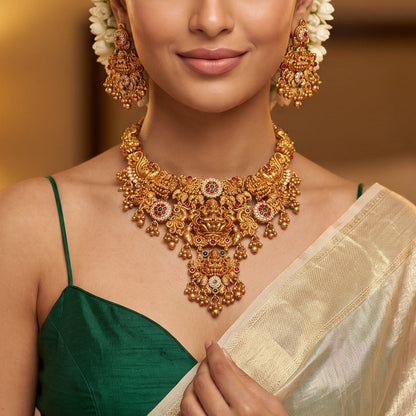 Avani Temple premium antique gold choker necklace featuring a broad central stacked pendant encrusted with pink and green kemp stones twin peacocks a gold ghungroo fringe and matching dome jhumka earrings
